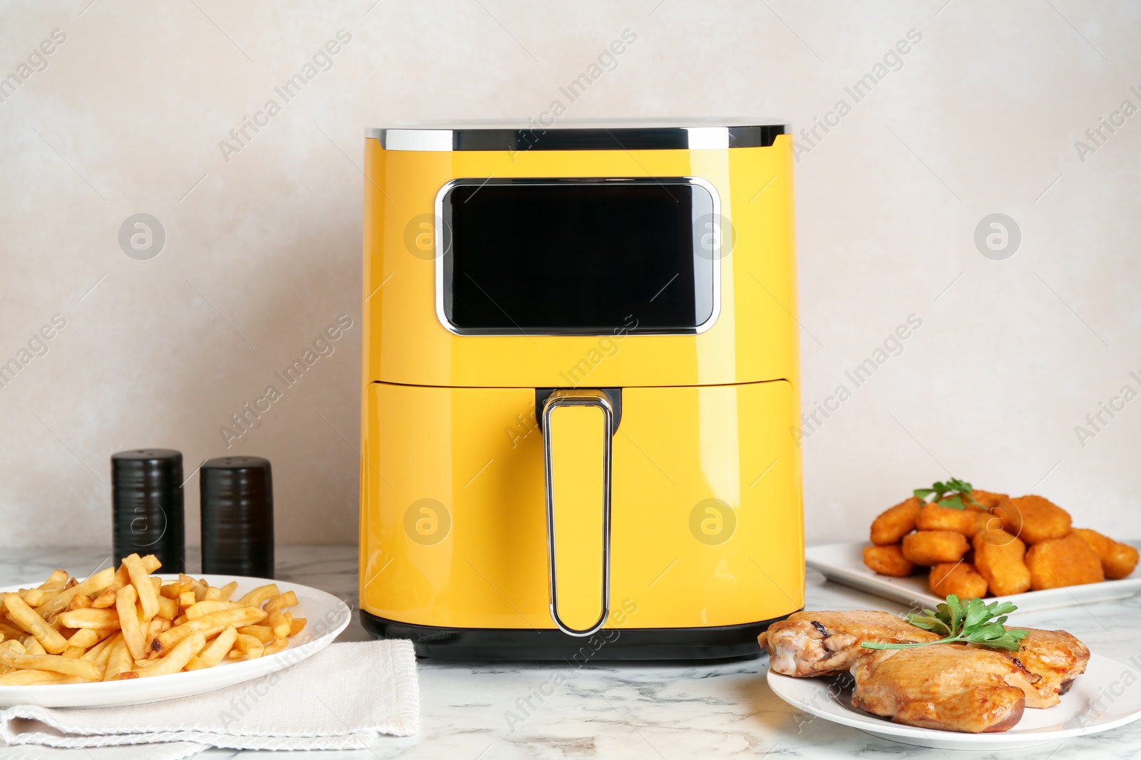 Photo of Modern air fryer and cooked meals on white marble table