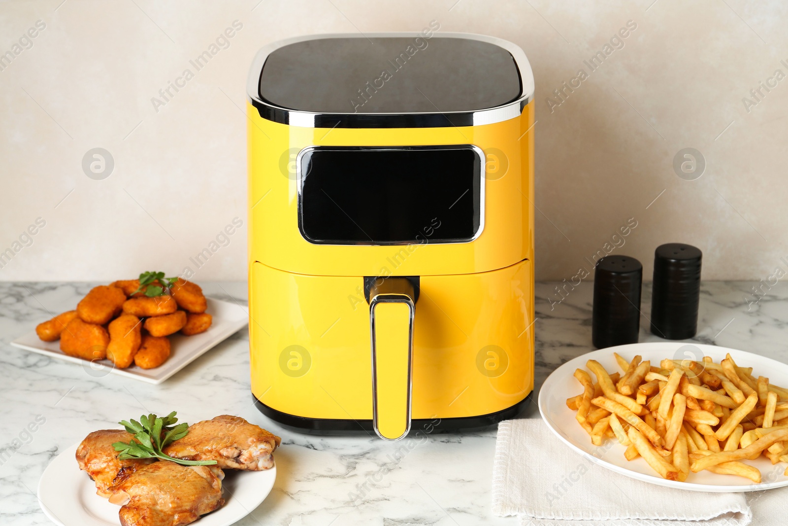Photo of Modern air fryer and cooked meals on white marble table