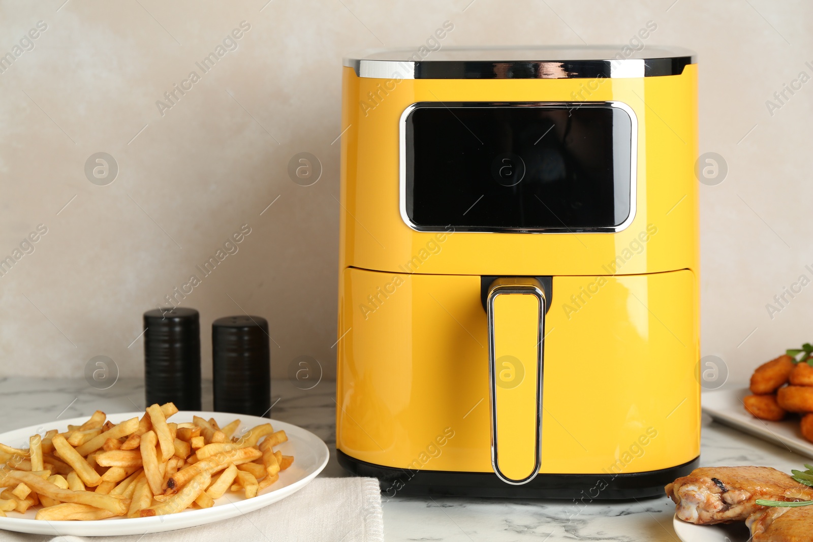 Photo of Modern air fryer and cooked meals on white marble table
