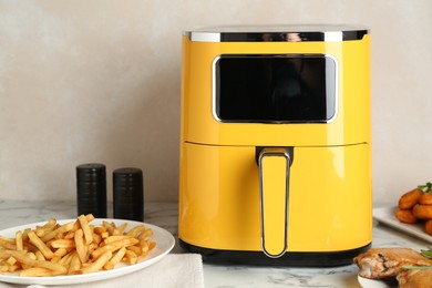 Photo of Modern air fryer and cooked meals on white marble table