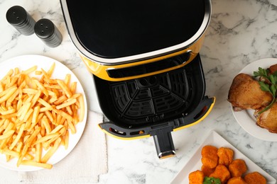 Photo of Air fryer and cooked meals on white marble table, flat lay