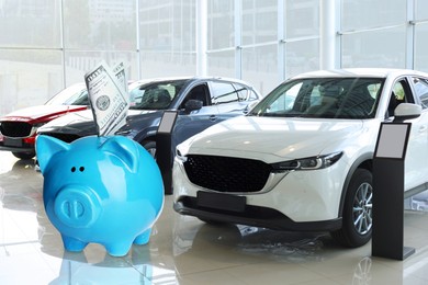 Image of Save money for car. Blue piggy bank with dollars in car dealership