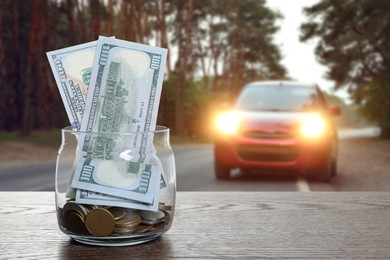 Image of Save money for car. Glass jar with cash on table against blurred automobile