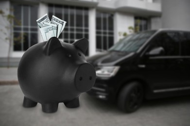Image of Save money for car. Black piggy bank with dollars against blurred automobile