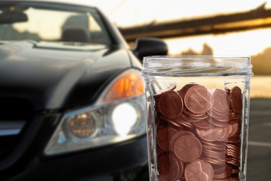 Image of Save money for car. Glass jar with coins against blurred automobile