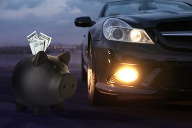 Image of Save money for car. Black piggy bank with dollars near automobile outdoors