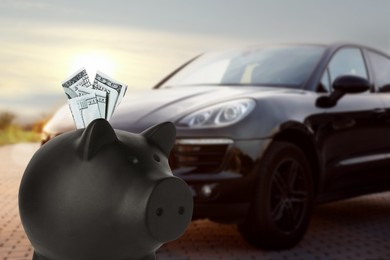 Image of Save money for car. Black piggy bank with dollars against blurred automobile