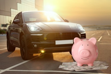 Image of Save money for car. Pink piggy bank and dollars near automobile outdoors