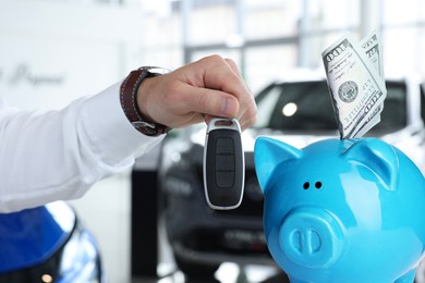 Image of Save money for car. Piggy bank with dollars and man holding car key indoors