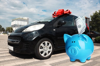 Image of Save money for car. Blue piggy bank with dollars near automobile outdoors