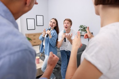 Photo of Young woman and man singing karaoke at home, selective focus