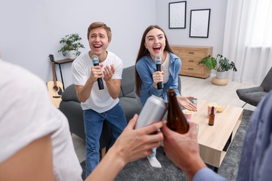 Photo of Young woman and man singing karaoke at home, selective focus