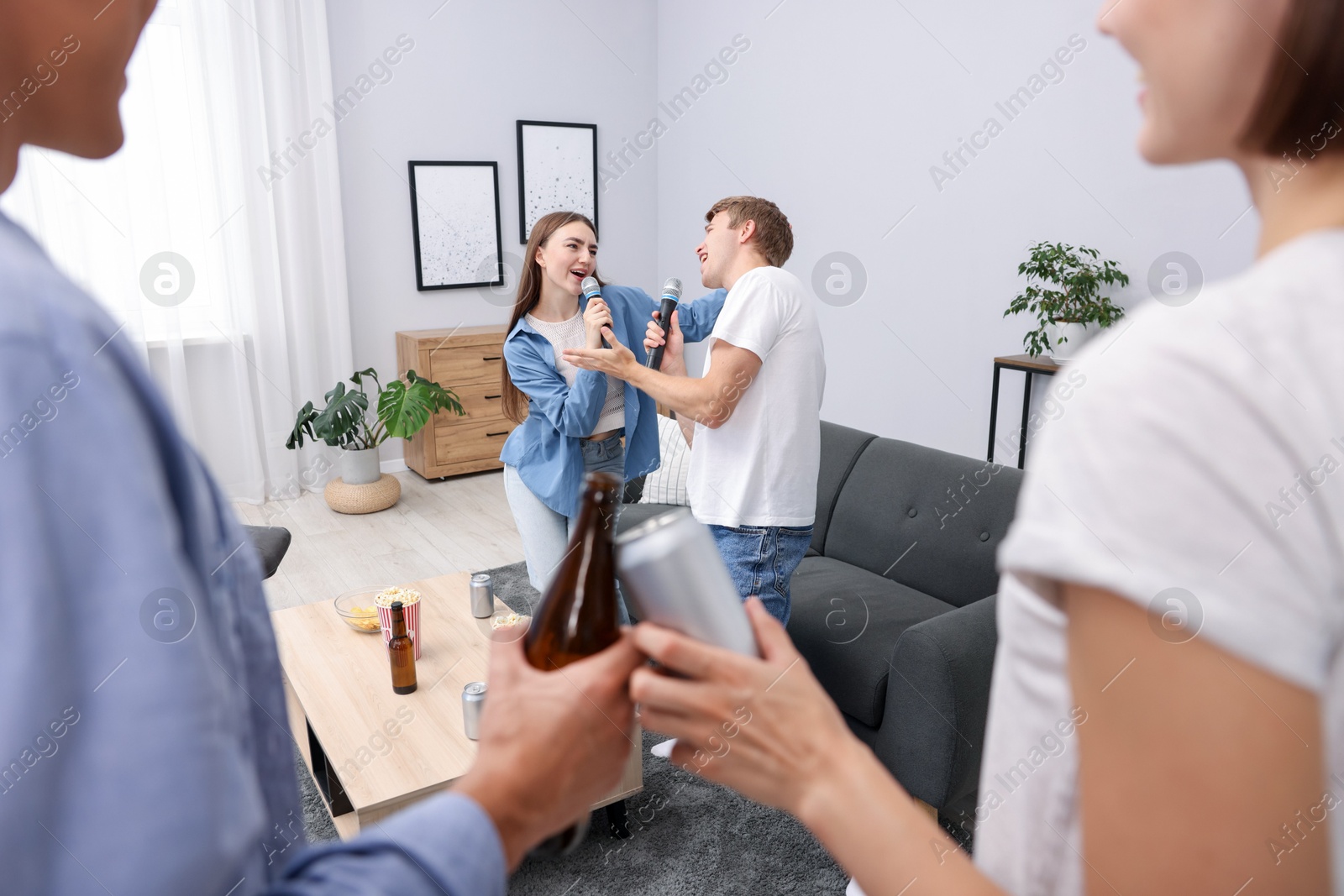 Photo of Young woman and man singing karaoke at home, selective focus