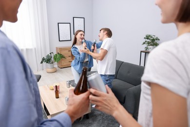 Photo of Young woman and man singing karaoke at home, selective focus