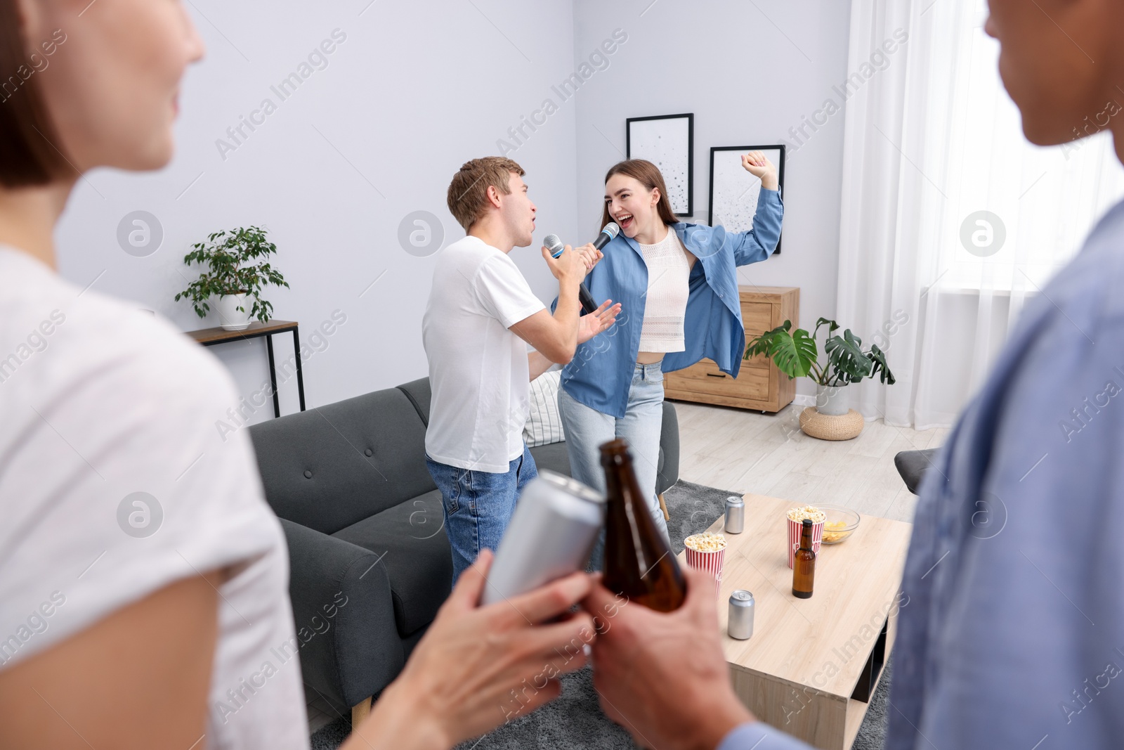 Photo of Young woman and man singing karaoke at home, selective focus