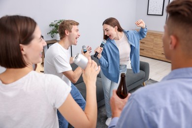 Photo of Young woman and man singing karaoke at home, selective focus