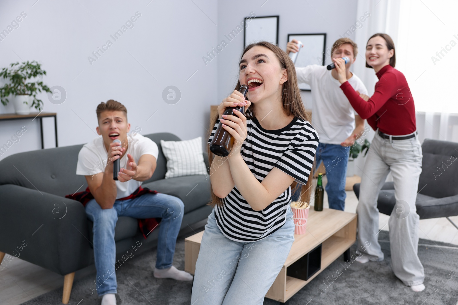 Photo of Young woman singing karaoke with friends at home, selective focus