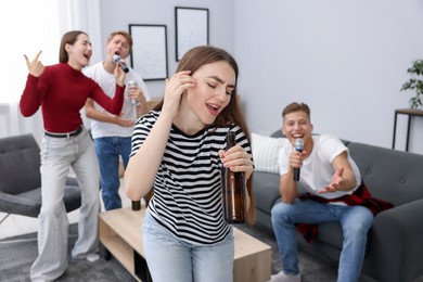Photo of Young woman singing karaoke with friends at home, selective focus