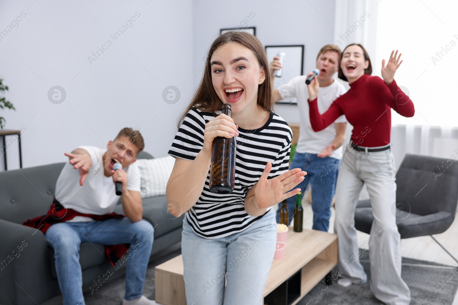 Photo of Young woman singing karaoke with friends at home, selective focus