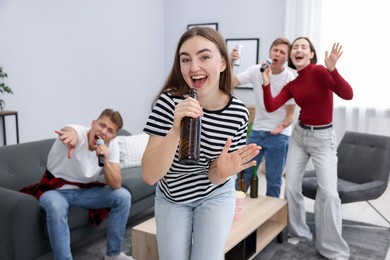 Photo of Young woman singing karaoke with friends at home, selective focus