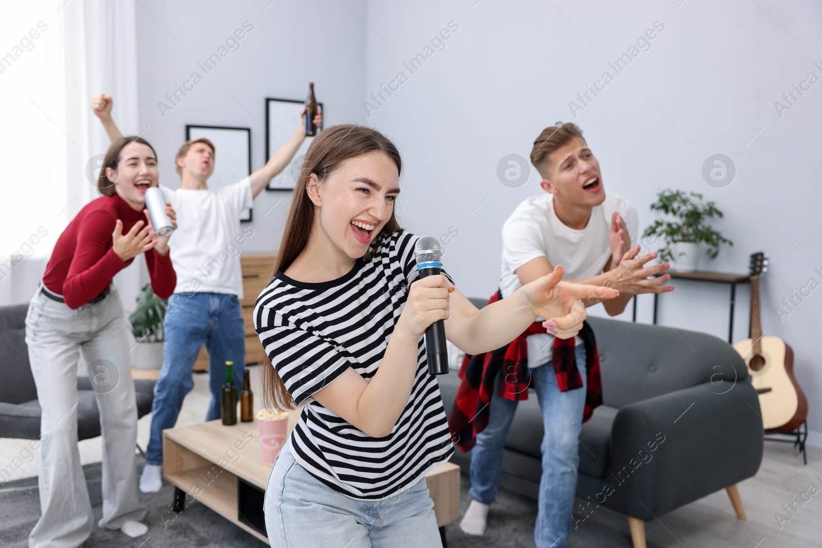 Photo of Young woman singing karaoke with friends at home, selective focus