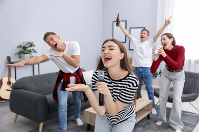 Photo of Young woman singing karaoke with friends at home, selective focus