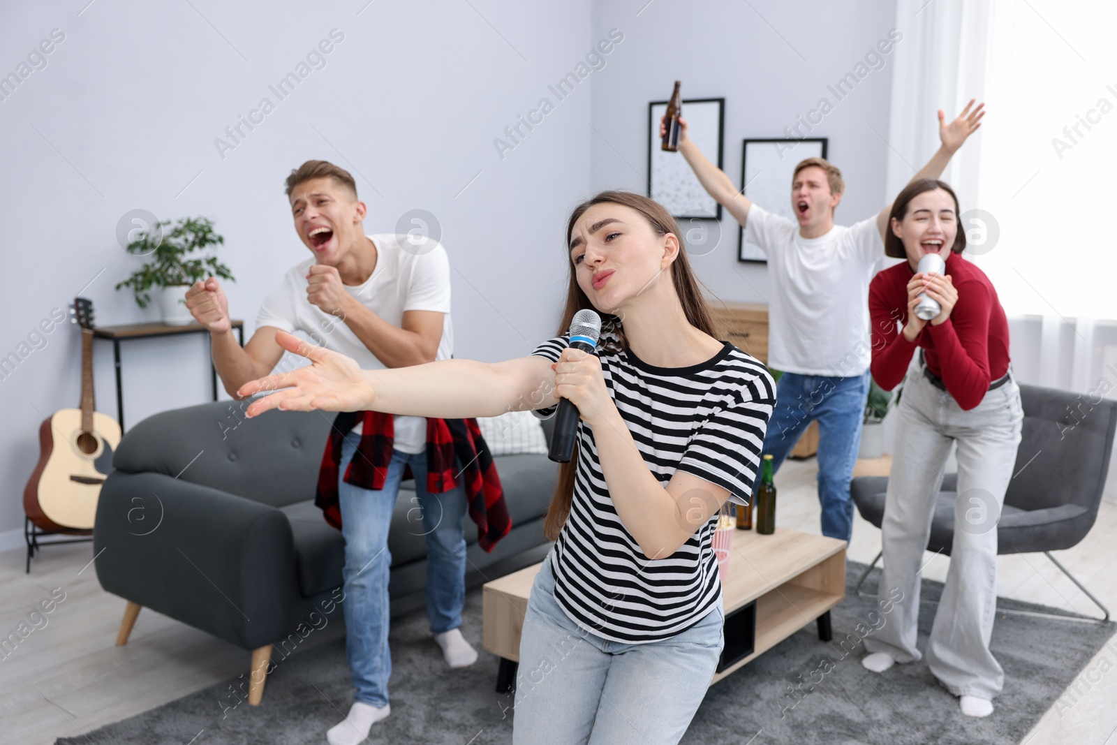 Photo of Young woman singing karaoke with friends at home, selective focus