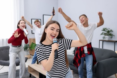 Photo of Young woman singing karaoke with friends at home, selective focus