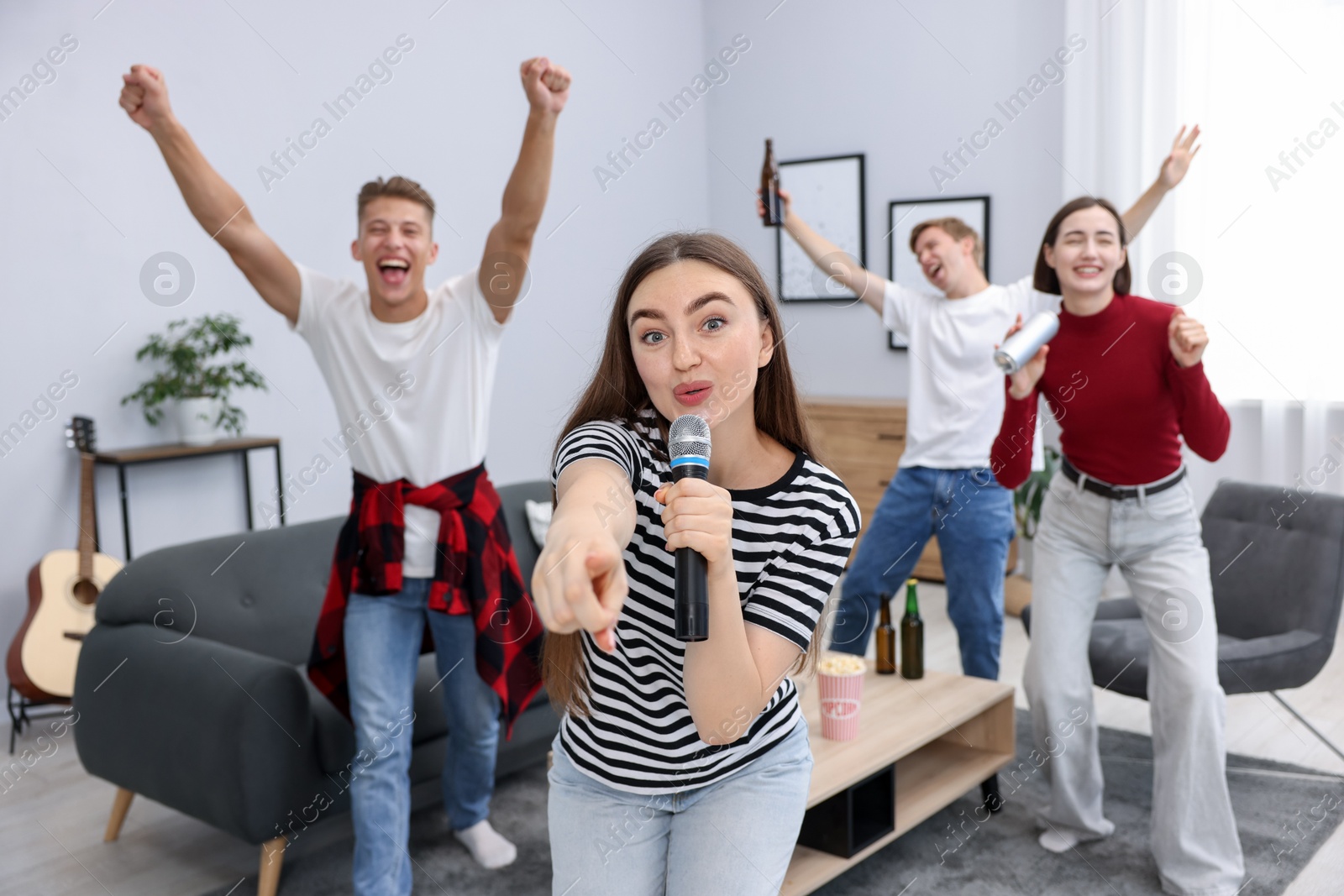 Photo of Young woman singing karaoke with friends at home, selective focus