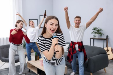 Photo of Young woman singing karaoke with friends at home, selective focus