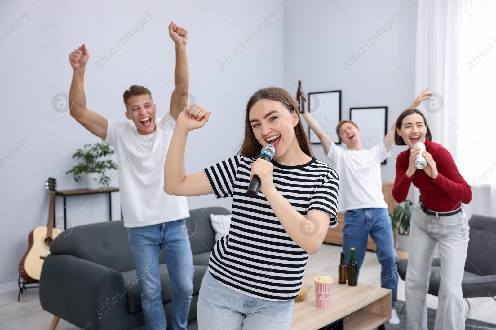 Photo of Young woman singing karaoke with friends at home, selective focus