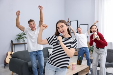 Photo of Young woman singing karaoke with friends at home, selective focus