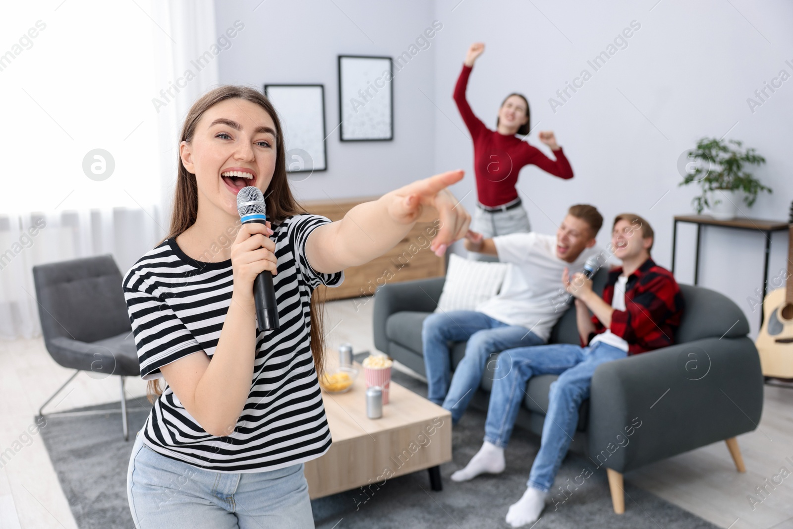 Photo of Young woman singing karaoke with friends at home, selective focus