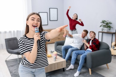 Photo of Young woman singing karaoke with friends at home, selective focus