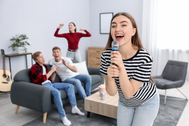 Photo of Young woman singing karaoke with friends at home, selective focus