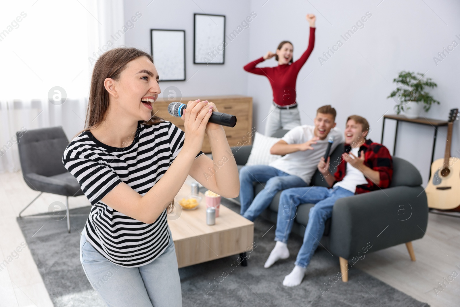 Photo of Young woman singing karaoke with friends at home, selective focus