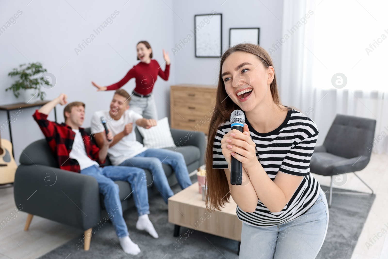 Photo of Young woman singing karaoke with friends at home, selective focus