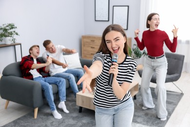 Photo of Young woman singing karaoke with friends at home, selective focus