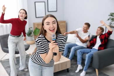 Photo of Young woman singing karaoke with friends at home, selective focus