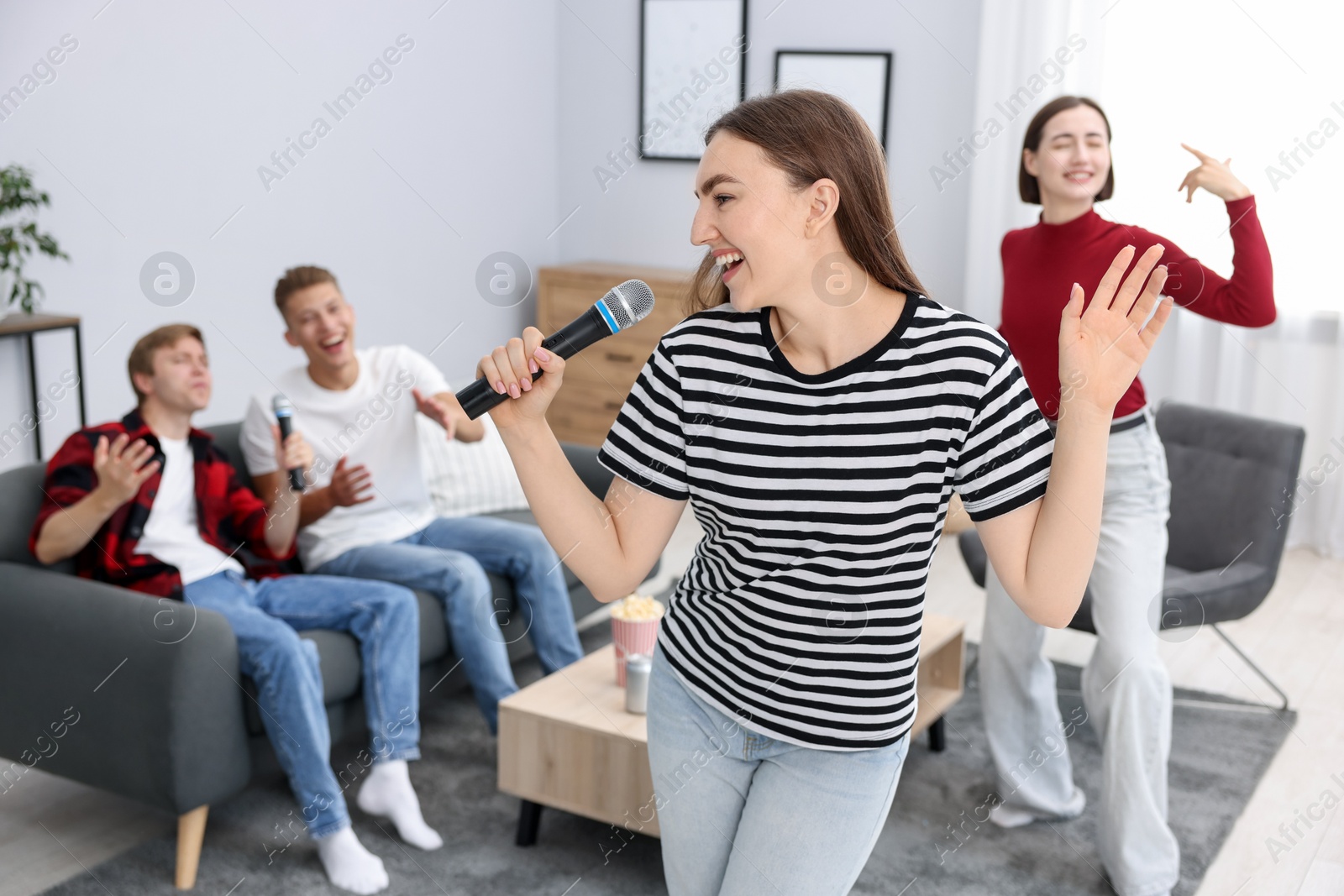 Photo of Young woman singing karaoke with friends at home, selective focus