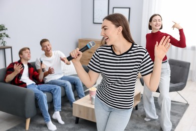 Photo of Young woman singing karaoke with friends at home, selective focus