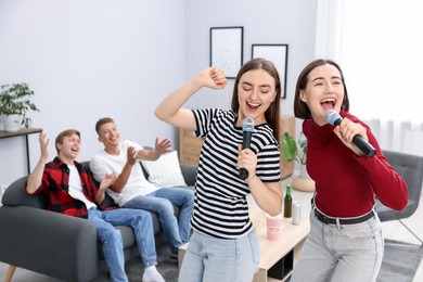 Photo of Young woman singing karaoke with friends at home, selective focus