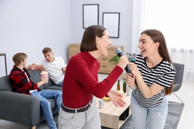 Photo of Young woman singing karaoke with friends at home, selective focus