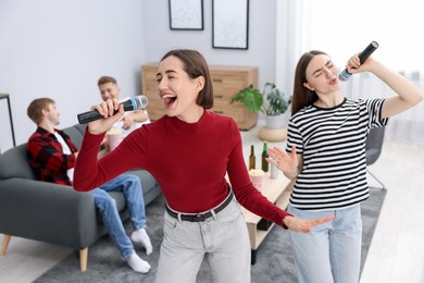 Photo of Young woman singing karaoke with friends at home, selective focus