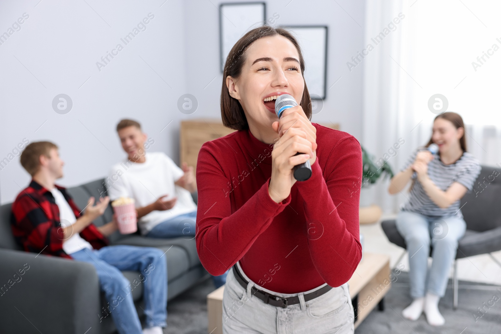 Photo of Young woman singing karaoke with friends at home, selective focus