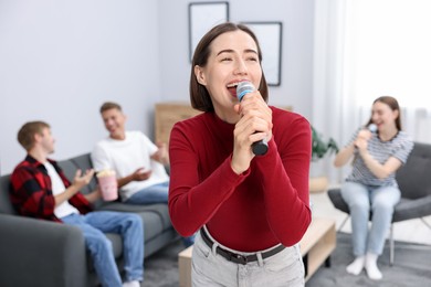 Photo of Young woman singing karaoke with friends at home, selective focus