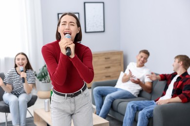 Photo of Young woman singing karaoke with friends at home, selective focus