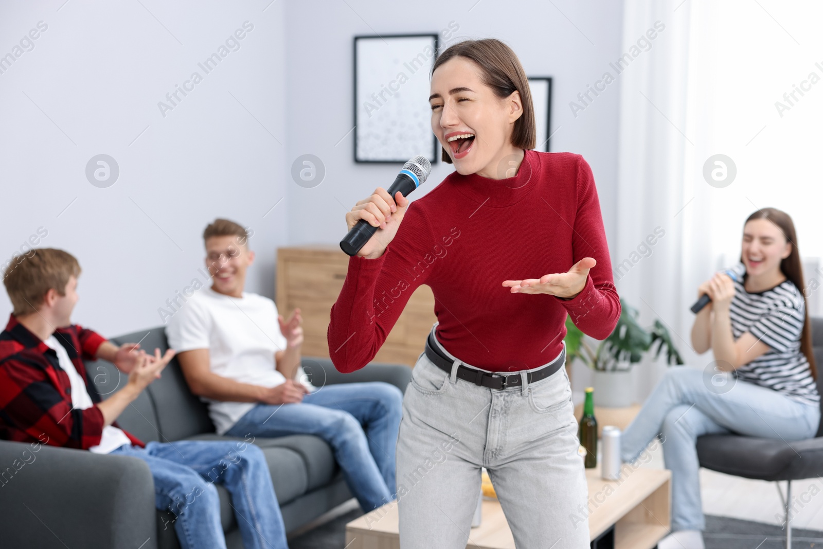 Photo of Young woman singing karaoke with friends at home, selective focus