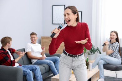 Photo of Young woman singing karaoke with friends at home, selective focus