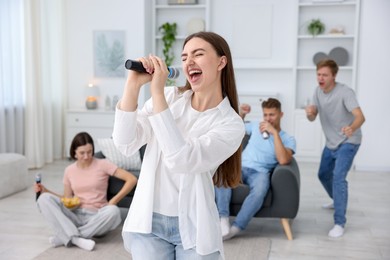 Photo of Young woman singing karaoke with friends at home, selective focus